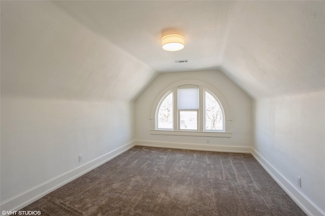 additional living space with dark carpet, baseboards, visible vents, and vaulted ceiling