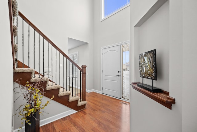 foyer entrance featuring visible vents, stairway, a high ceiling, wood finished floors, and baseboards