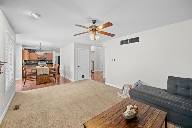 living room with a ceiling fan, visible vents, light carpet, and baseboards