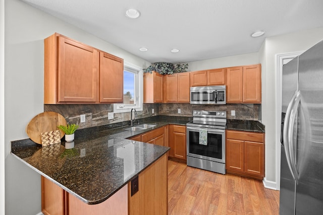 kitchen with backsplash, appliances with stainless steel finishes, a sink, light wood-type flooring, and a peninsula