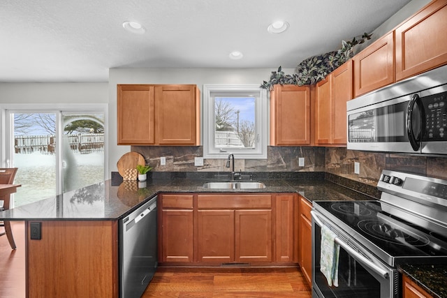 kitchen featuring tasteful backsplash, dark stone counters, appliances with stainless steel finishes, a peninsula, and a sink