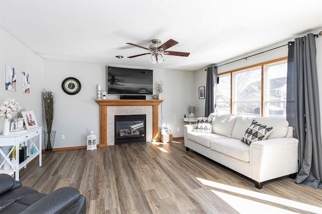 living area with a tiled fireplace, wood finished floors, a ceiling fan, and baseboards