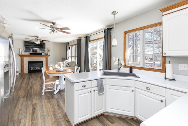 kitchen with a fireplace, stainless steel refrigerator with ice dispenser, light countertops, white cabinets, and a sink