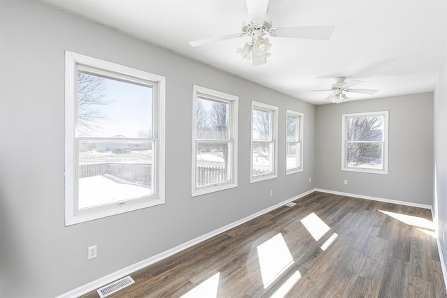 unfurnished room with a ceiling fan, dark wood-style flooring, visible vents, and baseboards