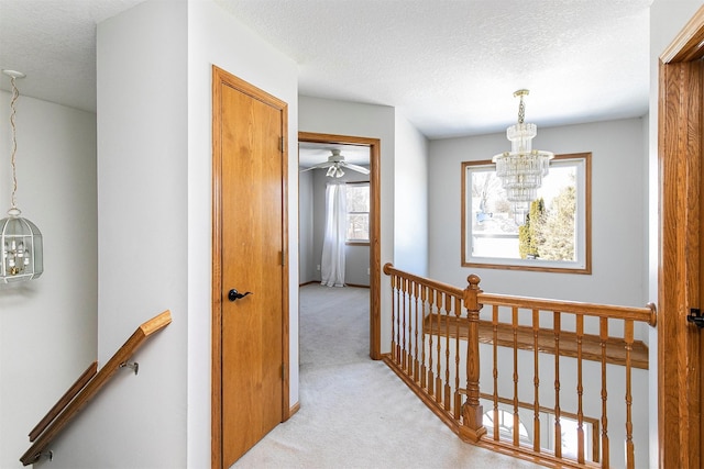 hallway featuring light carpet, a textured ceiling, an upstairs landing, and an inviting chandelier