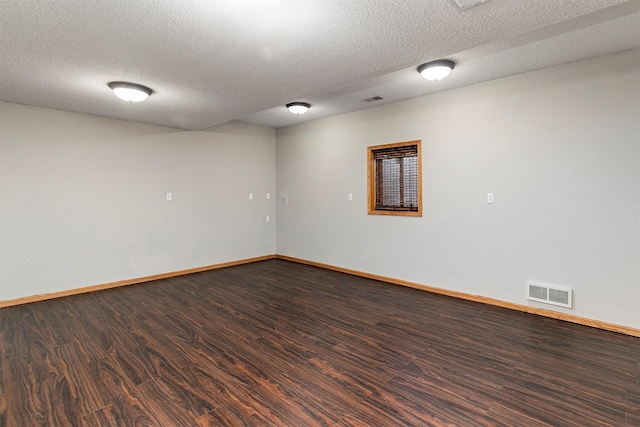 empty room featuring dark wood-type flooring, visible vents, a textured ceiling, and baseboards