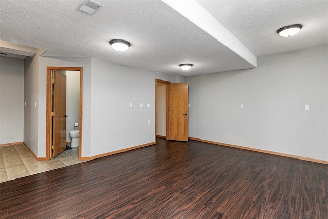 basement with a textured ceiling, wood finished floors, visible vents, and baseboards