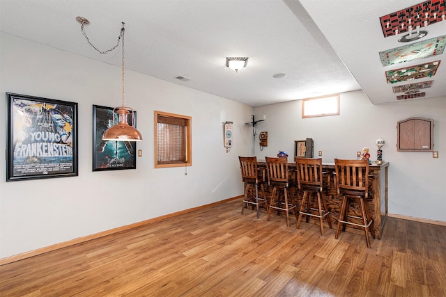 dining space featuring baseboards, a textured ceiling, a dry bar, and wood finished floors