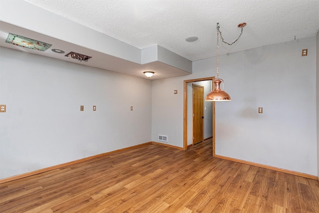 unfurnished room featuring a textured ceiling, light wood-type flooring, visible vents, and baseboards