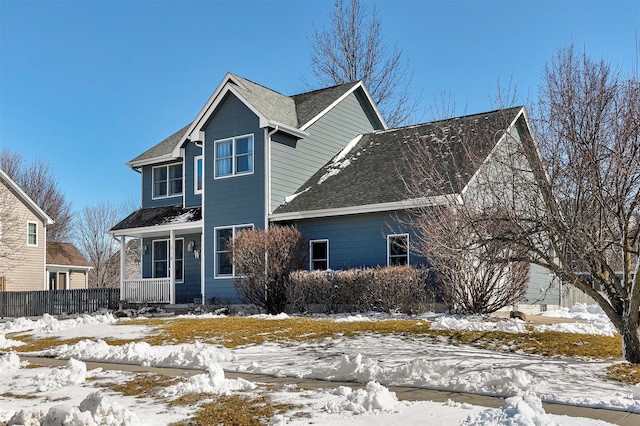 snow covered rear of property with covered porch and roof with shingles