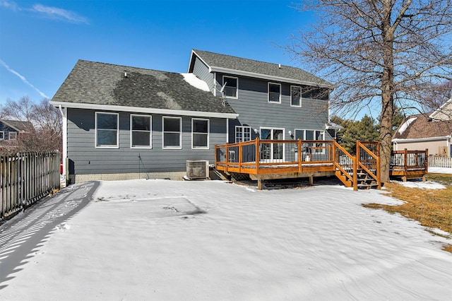 snow covered back of property featuring a deck, central AC, a shingled roof, and fence