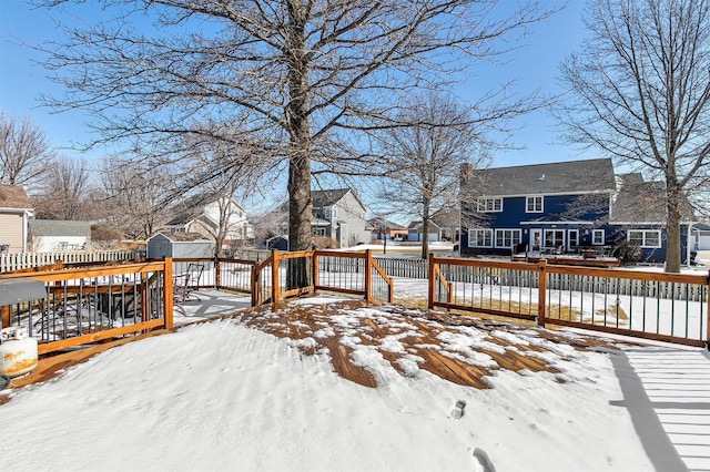 snow covered deck with a residential view, fence, a storage unit, and an outdoor structure