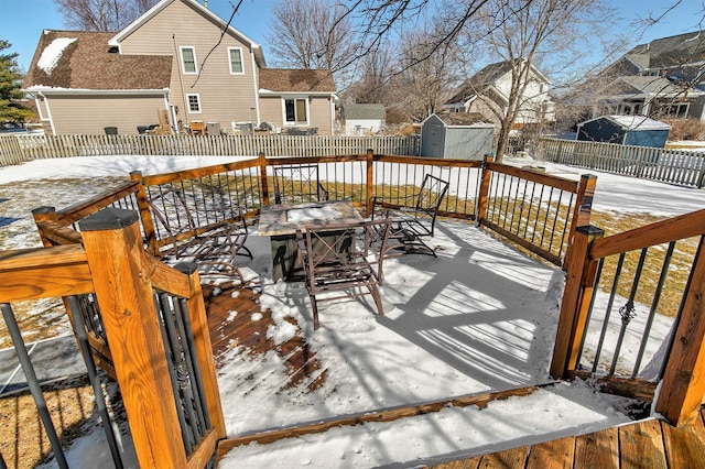 snow covered deck featuring a shed, an outdoor structure, a fenced backyard, and a residential view