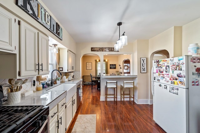 kitchen with arched walkways, dark wood-type flooring, freestanding refrigerator, a sink, and backsplash