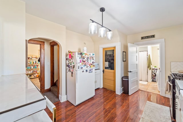 502 E Douglas St, Knoxville, IA 50138 - kitchen featuring freestanding refrigerator, stainless steel gas range oven, arched walkways, dark wood finished floors, and hanging light fixtures