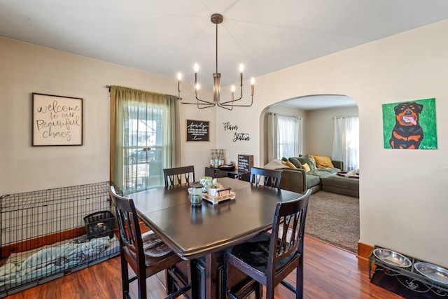 dining room with dark wood-style floors, arched walkways, and a notable chandelier