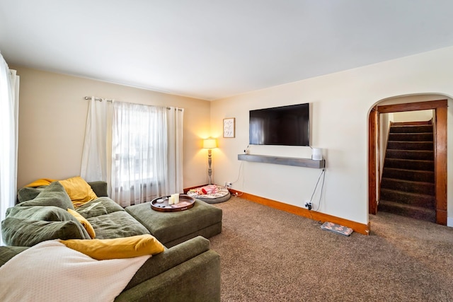 carpeted living room featuring arched walkways, baseboards, and stairs