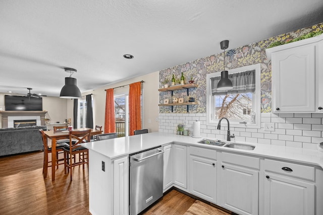 kitchen featuring a peninsula, wood finished floors, a sink, stainless steel dishwasher, and a glass covered fireplace