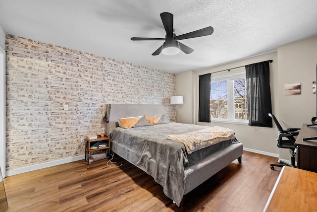 bedroom featuring a ceiling fan, a textured ceiling, baseboards, and wood finished floors