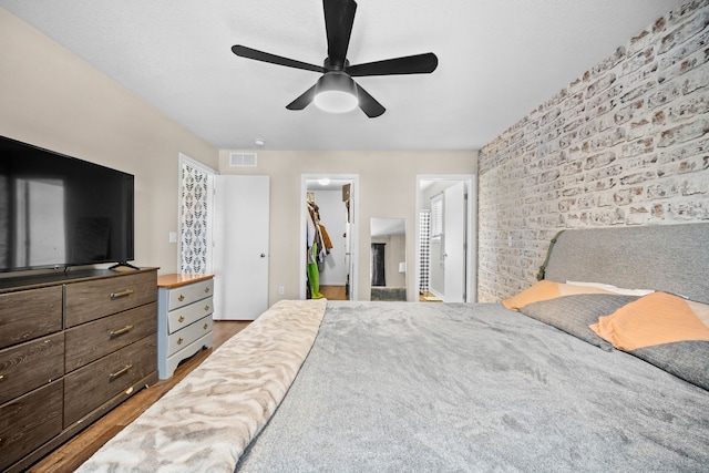 bedroom with a closet, visible vents, a spacious closet, brick wall, and wood finished floors