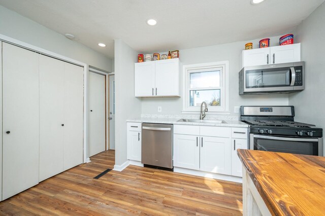 kitchen with a sink, appliances with stainless steel finishes, white cabinets, light wood finished floors, and wooden counters