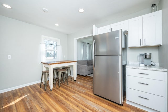 kitchen with light wood-style flooring, recessed lighting, white cabinetry, baseboards, and freestanding refrigerator