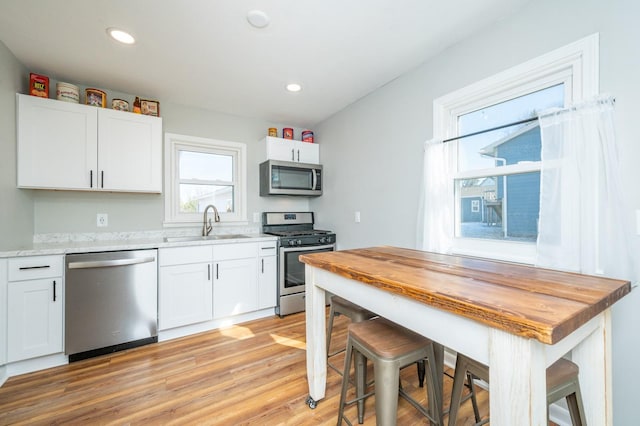 kitchen with stainless steel appliances, light wood-type flooring, a sink, and white cabinetry