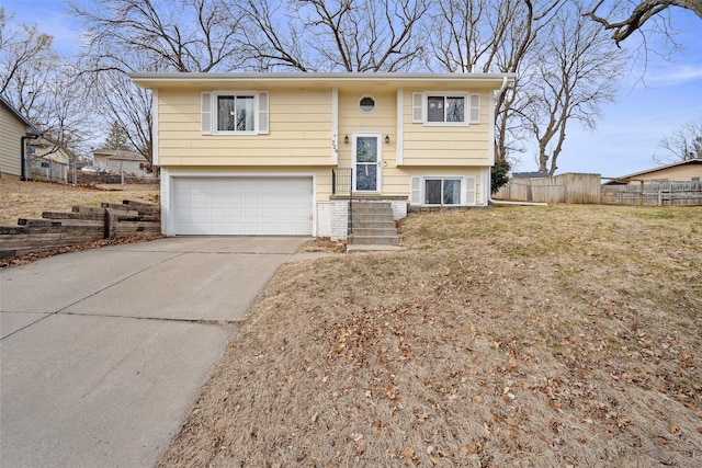 split foyer home featuring concrete driveway, an attached garage, and fence