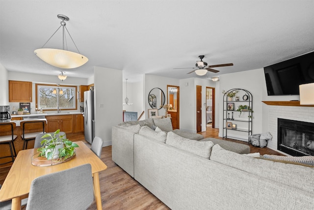 living room with a ceiling fan, light wood-type flooring, a fireplace, and baseboards