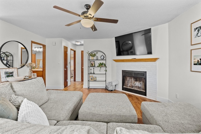 living room with ceiling fan, a brick fireplace, wood finished floors, and baseboards