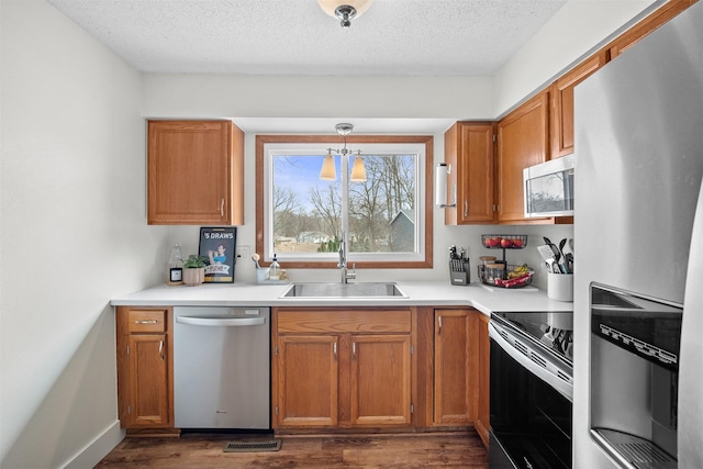 kitchen featuring brown cabinetry, appliances with stainless steel finishes, dark wood-type flooring, a textured ceiling, and a sink