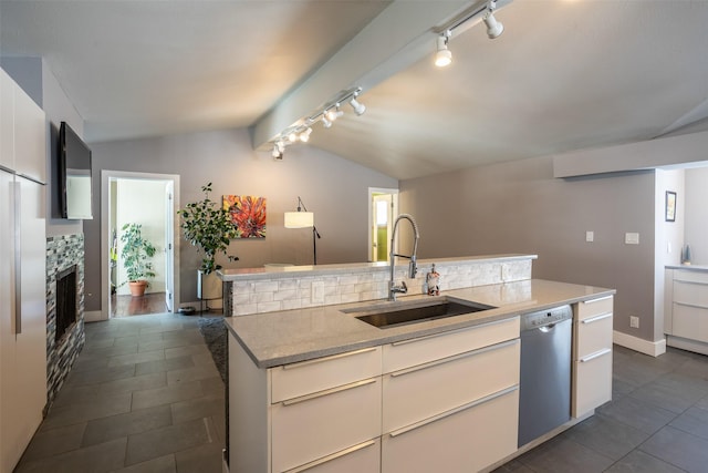 kitchen featuring a fireplace, stainless steel dishwasher, white cabinetry, vaulted ceiling, and a sink