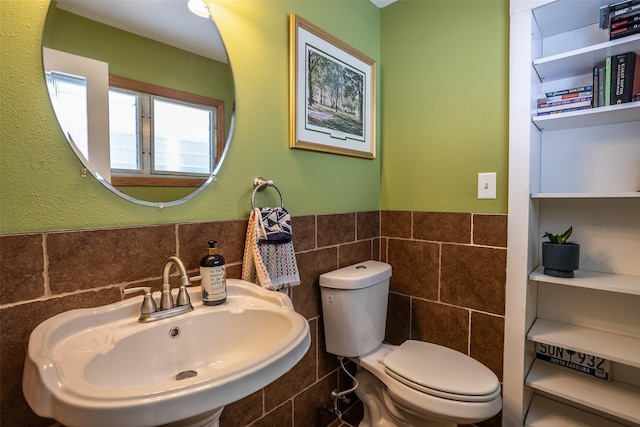 bathroom featuring a sink, toilet, tile walls, and wainscoting