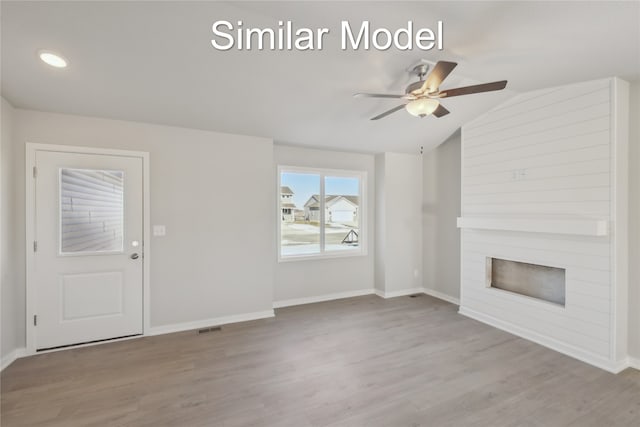 unfurnished living room with a large fireplace, wood finished floors, visible vents, baseboards, and vaulted ceiling