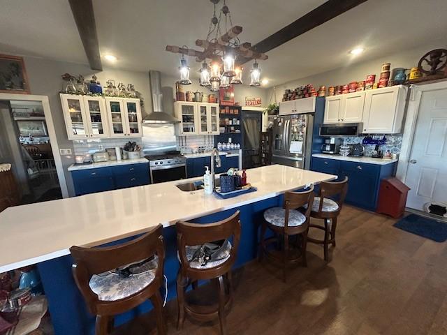 kitchen featuring dark wood-style flooring, a sink, appliances with stainless steel finishes, decorative backsplash, and wall chimney exhaust hood