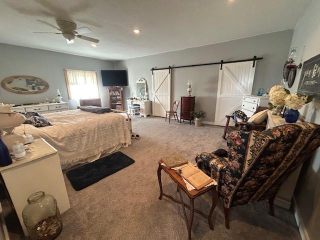 carpeted bedroom featuring a barn door and a ceiling fan