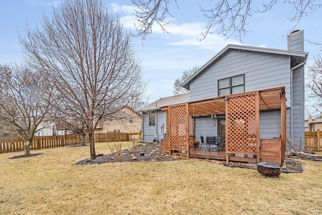 rear view of property with a chimney, a lawn, fence, a deck, and a fire pit