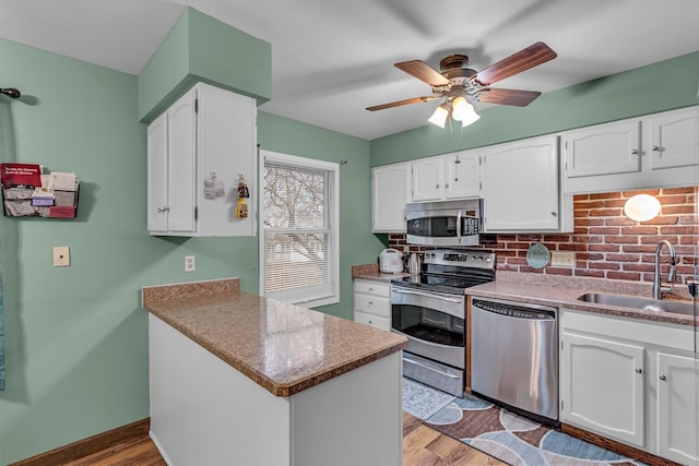 kitchen with wood finished floors, a peninsula, stainless steel appliances, white cabinetry, and a sink