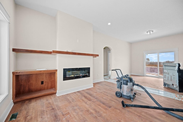 exercise area featuring arched walkways, wood finished floors, visible vents, baseboards, and a glass covered fireplace