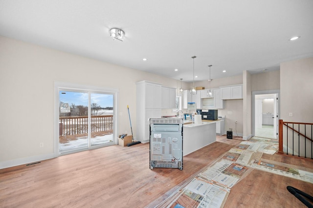 kitchen with black microwave, white cabinets, light countertops, light wood-type flooring, and a center island with sink