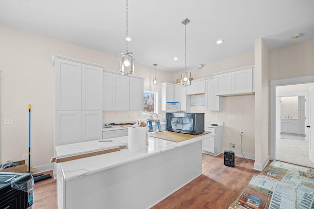 kitchen featuring light wood finished floors, black microwave, a center island, white cabinetry, and pendant lighting