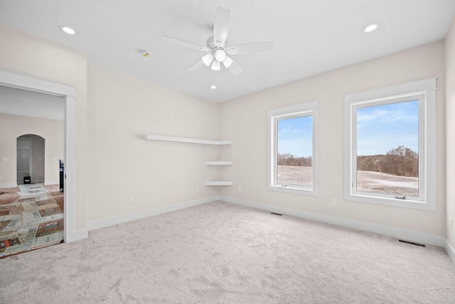 unfurnished room featuring arched walkways, visible vents, a ceiling fan, carpet flooring, and baseboards