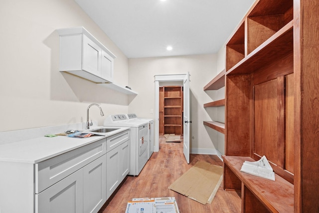 laundry area featuring cabinet space, light wood-style flooring, a sink, separate washer and dryer, and baseboards