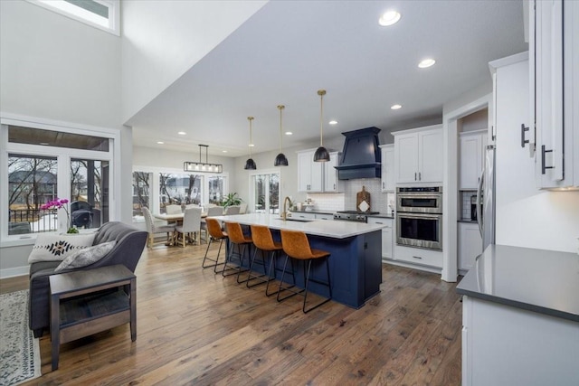 kitchen featuring dark wood finished floors, double oven, custom range hood, white cabinetry, and a sink