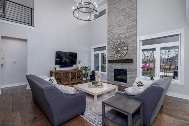 living area featuring a notable chandelier, hardwood / wood-style floors, a high ceiling, a fireplace, and baseboards