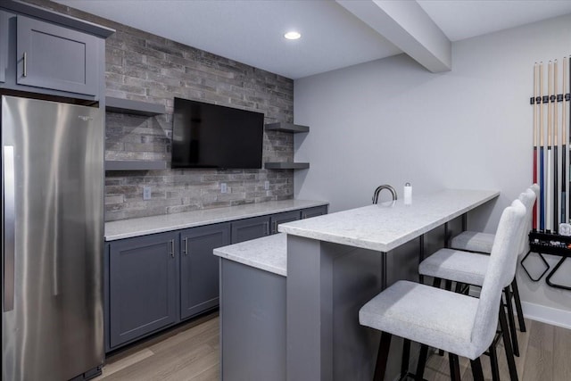 kitchen with light wood finished floors, backsplash, a breakfast bar area, freestanding refrigerator, and open shelves