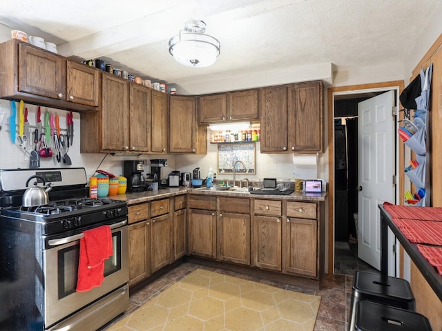 kitchen with brown cabinets, a sink, a textured ceiling, gas range, and beamed ceiling