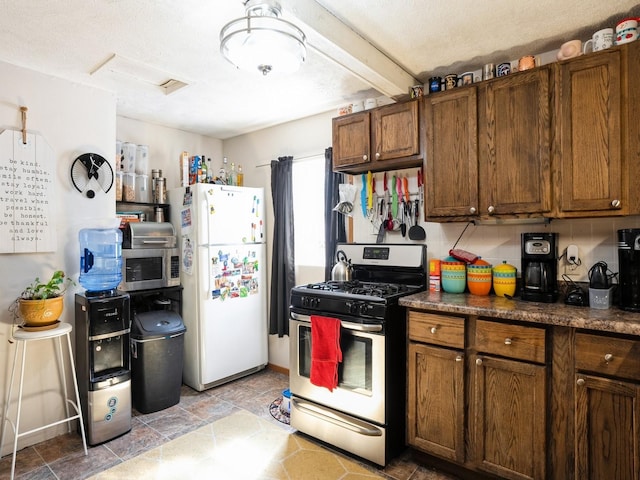 kitchen featuring stainless steel appliances, dark countertops, stone finish floor, and brown cabinets