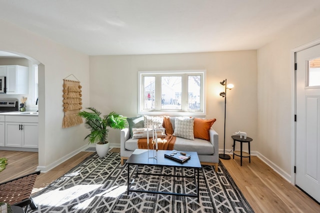 living area with light wood finished floors, plenty of natural light, arched walkways, and baseboards