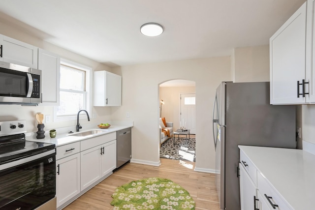 kitchen featuring arched walkways, light wood-style flooring, appliances with stainless steel finishes, light countertops, and a sink